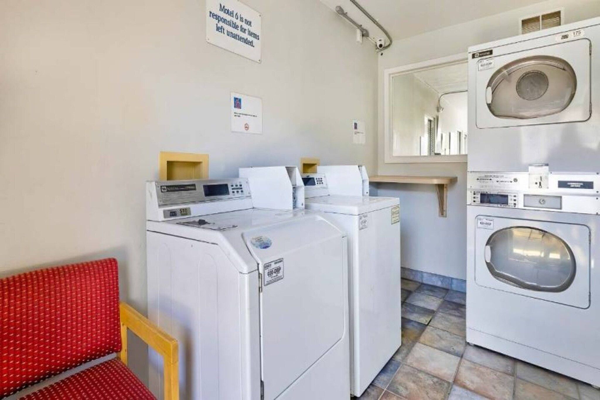 A laundry room with two washing machines, a dryer, and a red chair.
