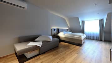 A modern hotel room with a sofa, a bed, a bedside table, and a window with curtains.