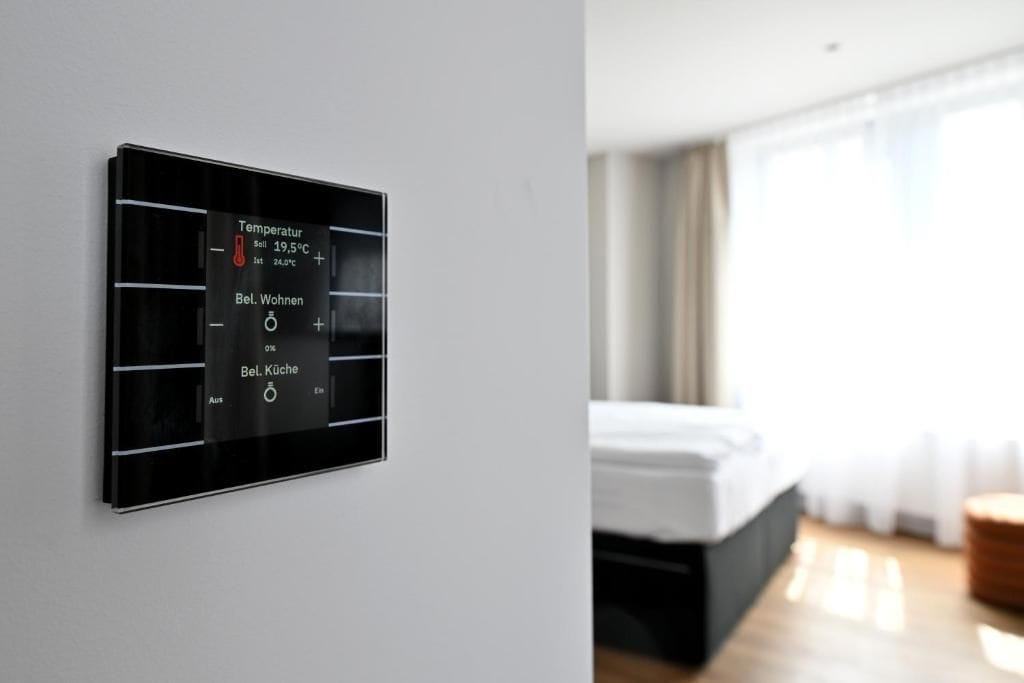 En termostat på väggen med temperaturinställningar och en kontrollpanel för att justera inställningarna för rummet och badrummet.