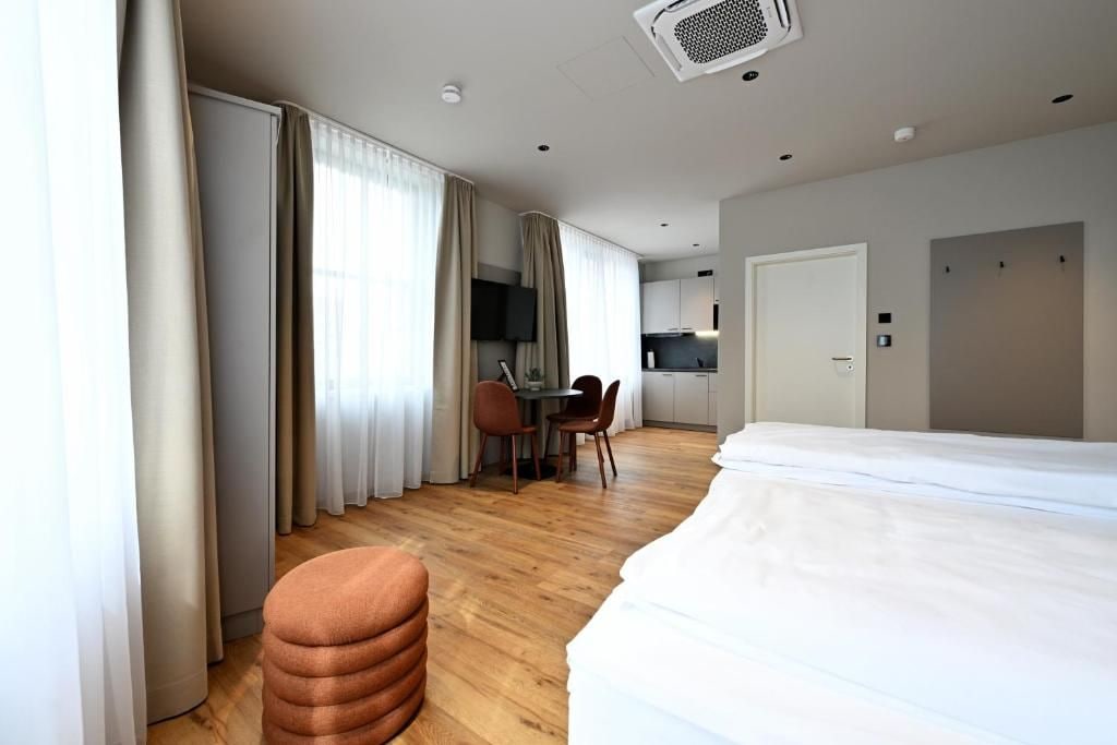 Et hotelværelse med en seng, et skrivebord med stole, et fjernsyn og et tekøkken i baggrunden.