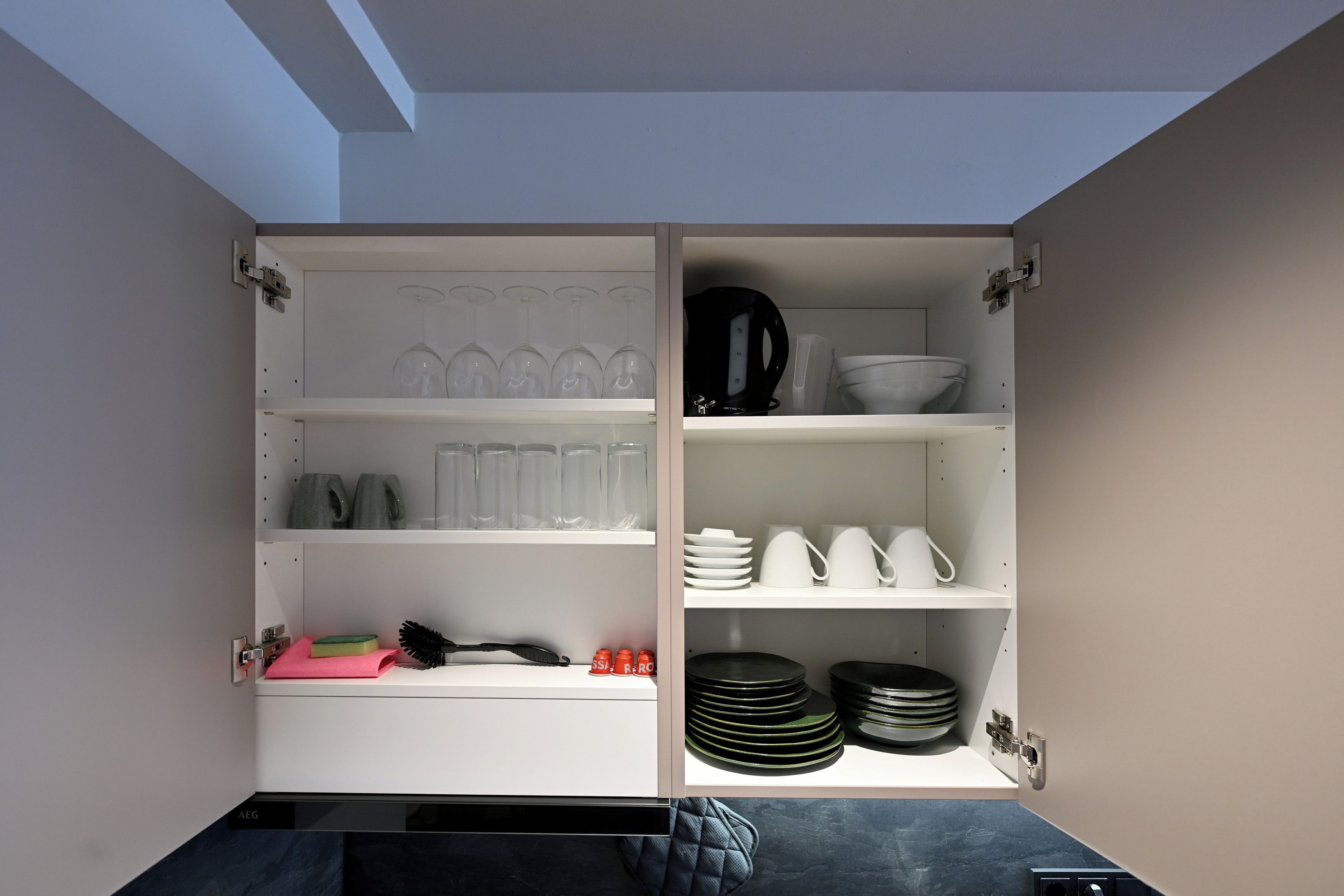 Una cocina con estantes abiertos, que contiene varios platos, vasos y utensilios de cocina.