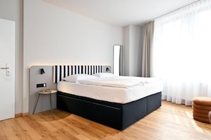 Ein modernes Schlafzimmer mit einem schwarz-weiß gestreiften Kopfteil, einem kleinen Nachttisch und einem großen Spiegel.