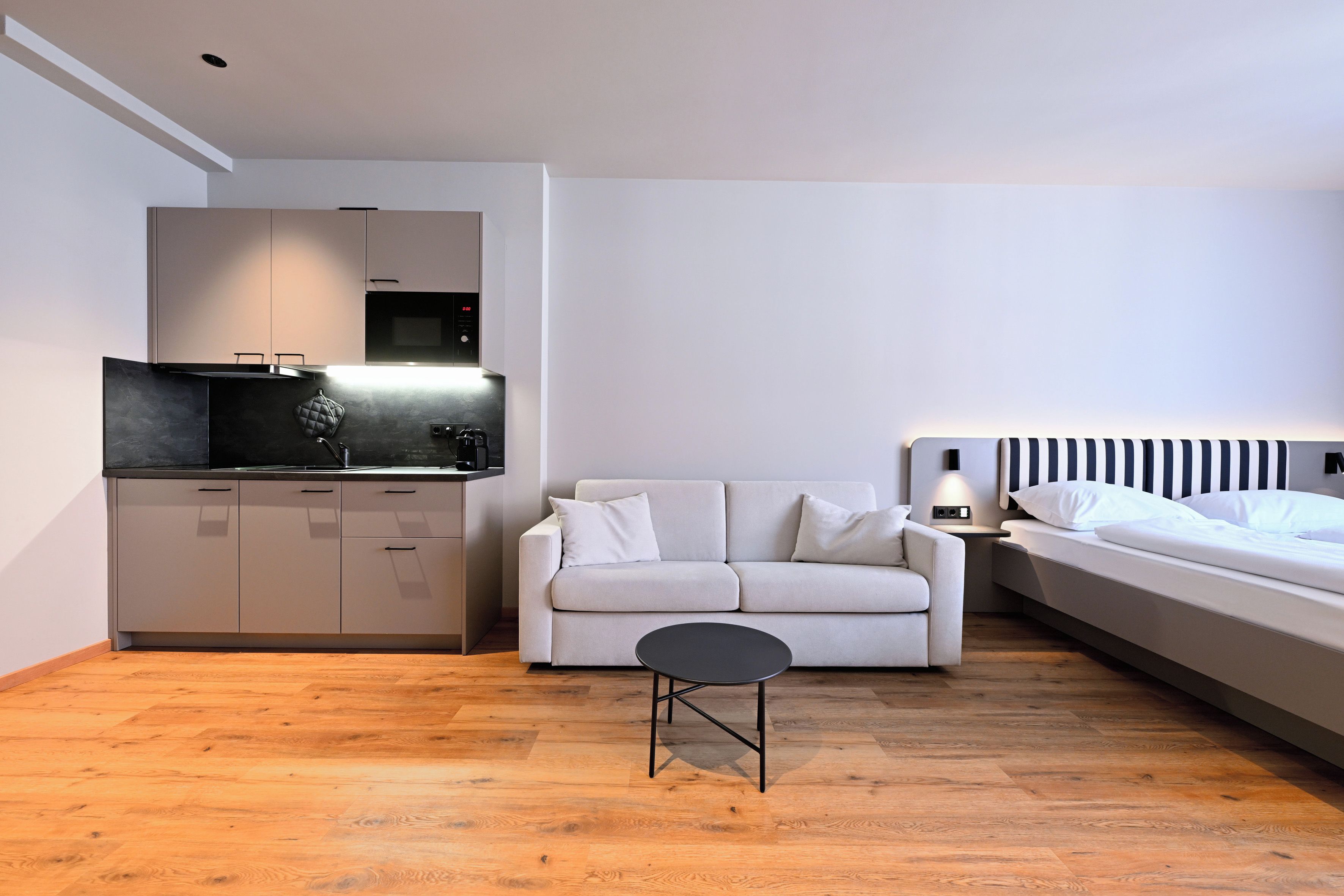 A modern, compact living space with a kitchenette, a sofa, a small table, and a bed.