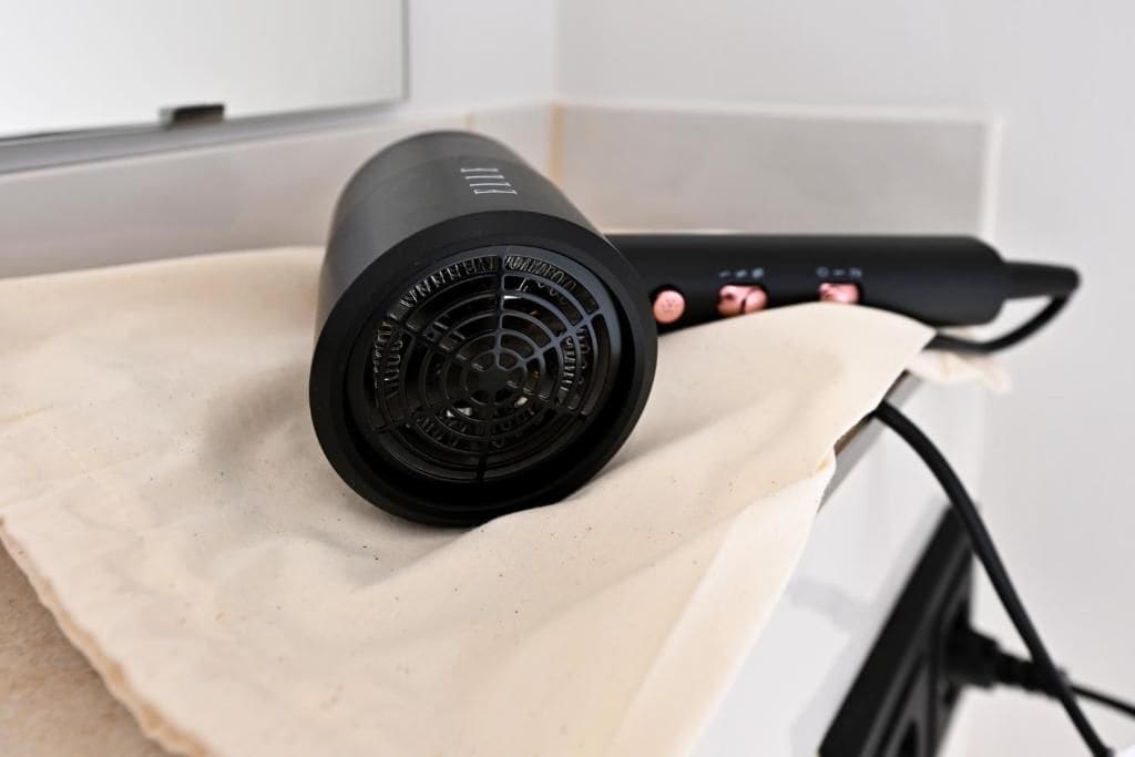 A hair dryer with a cord and a power strip on a beige surface.