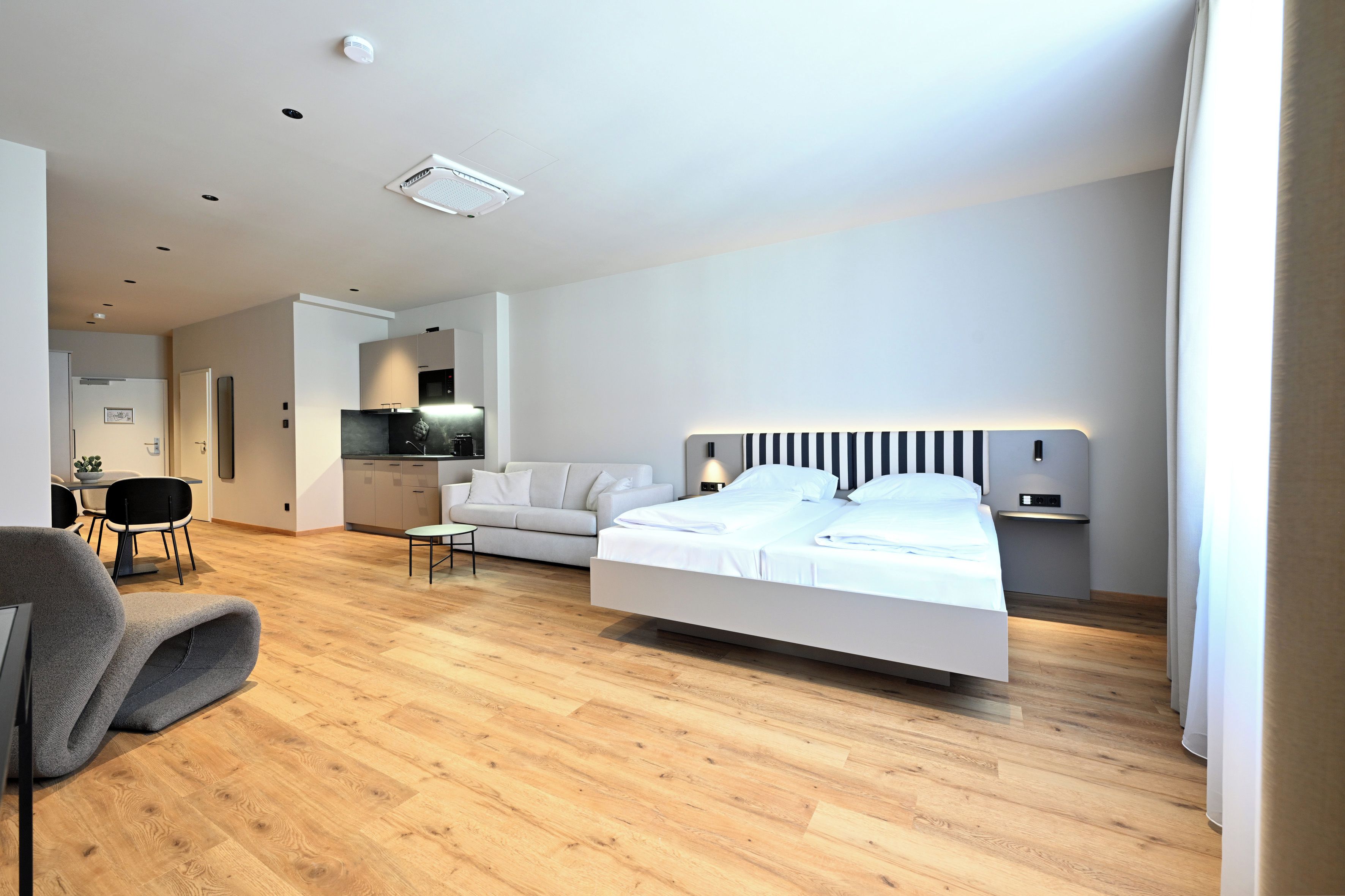 A modern bedroom with a bed, a sofa, a dining table, and a kitchen area.