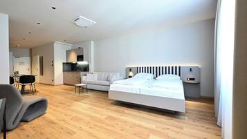 A modern bedroom with a bed, a sofa, a dining table, and a kitchen area.