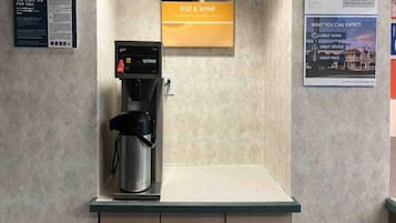 A coffee machine on a countertop with a sign above it that reads 'RISE & SHINE'.