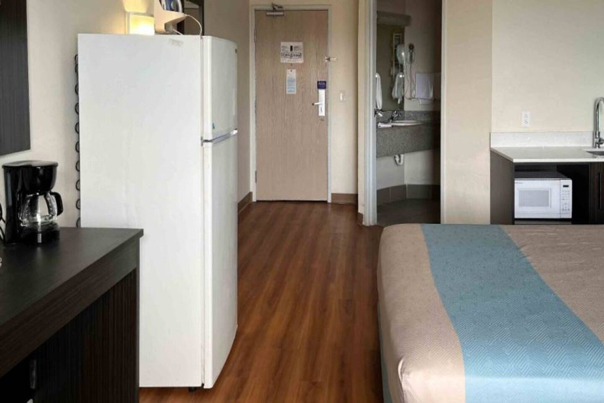 A hotel room with a bed, a kitchenette, a refrigerator, and a coffee maker.