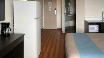 A hotel room with a bed, a kitchenette, a refrigerator, and a coffee maker.