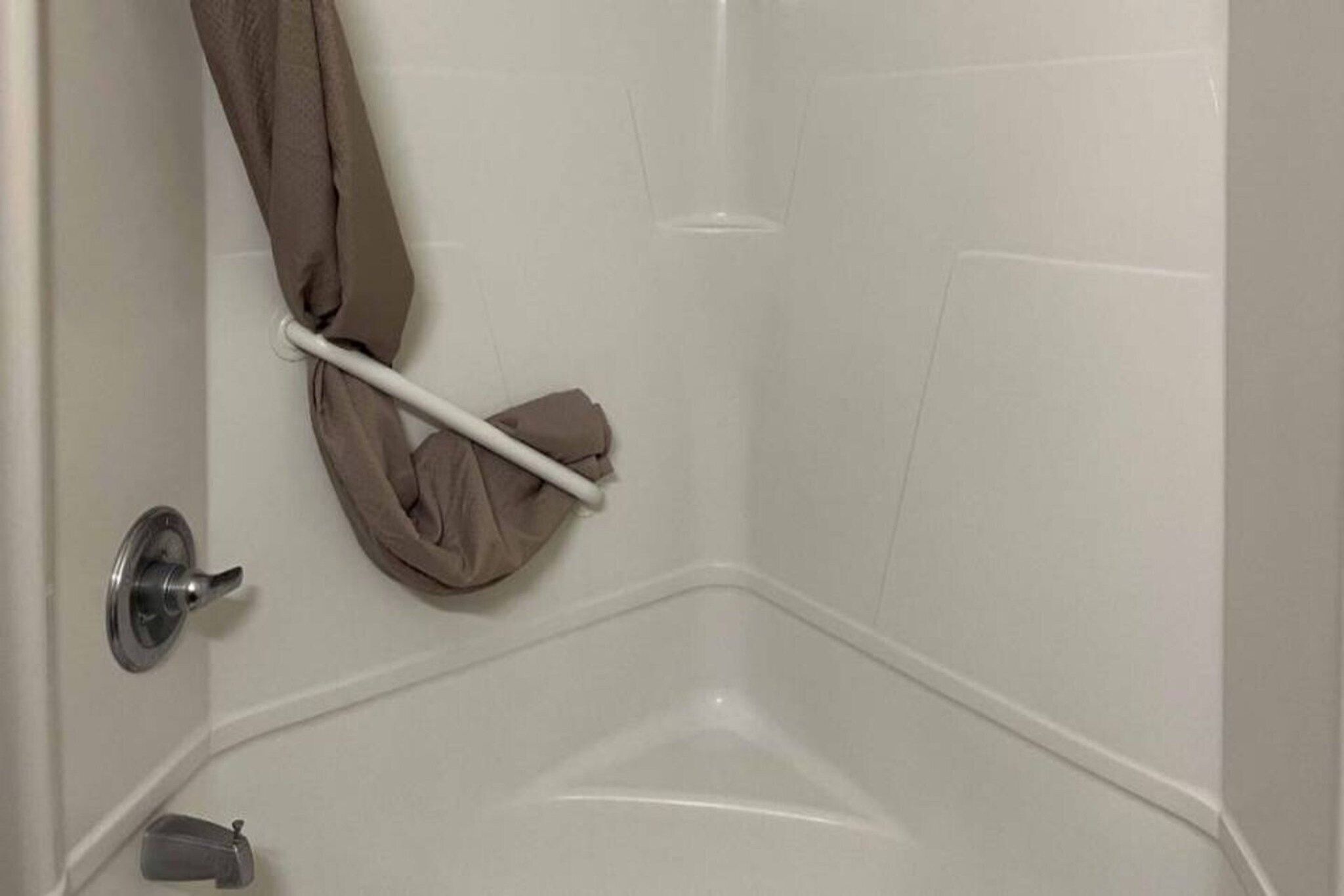 A corner of a bathroom with a white bathtub, a towel rack with a towel, and a door with a metallic handle.