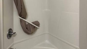 A corner of a bathroom with a white bathtub, a towel rack with a towel, and a door with a metallic handle.