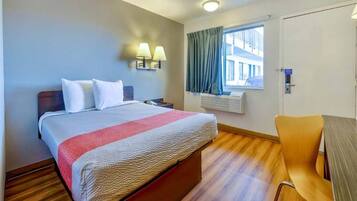 A hotel room with a bed, bedside lamps, a window with curtains, a desk, and a chair.