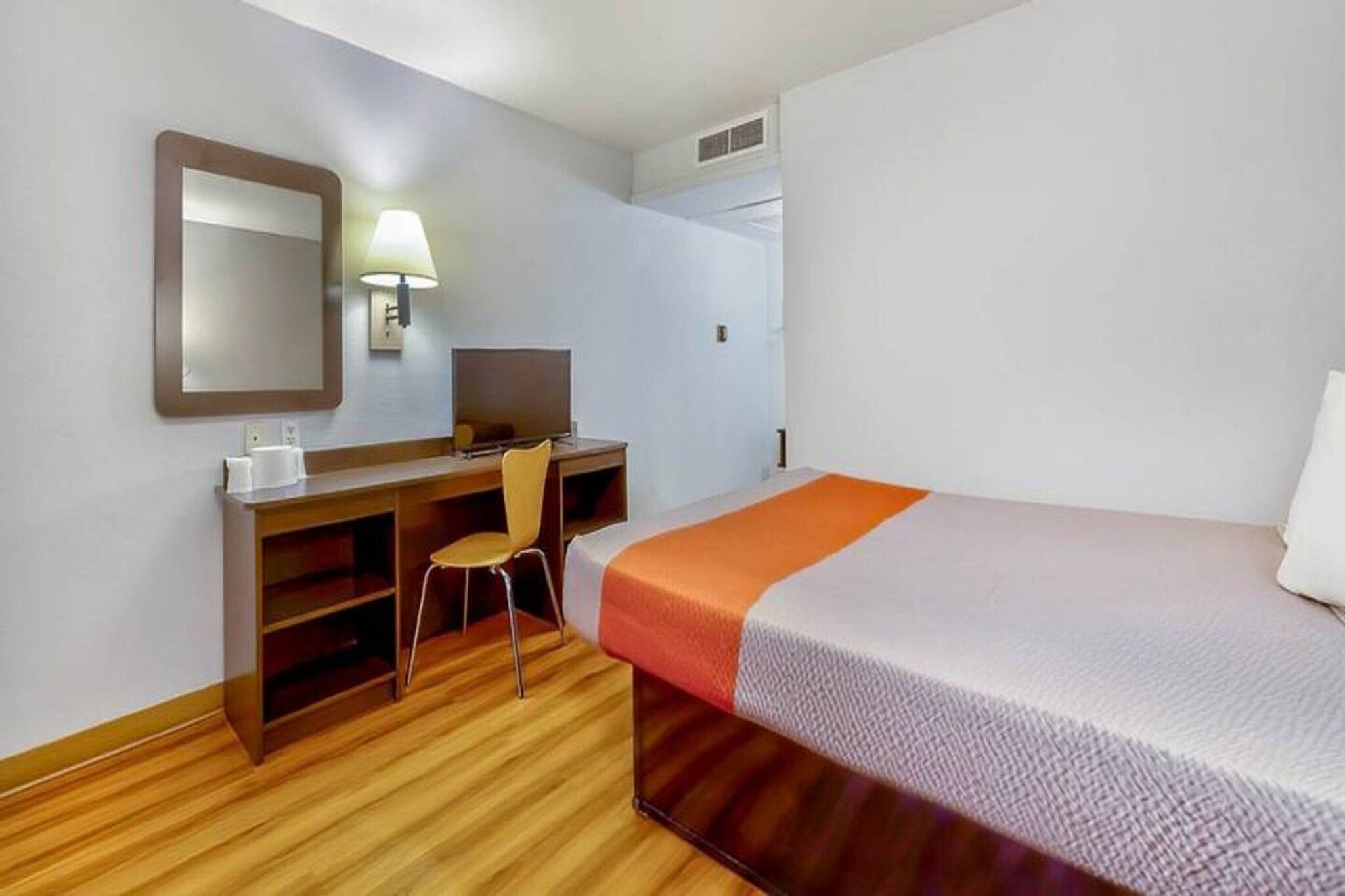 Quarto de hotel com cama, escrivaninha, cadeira, abajur e espelho.