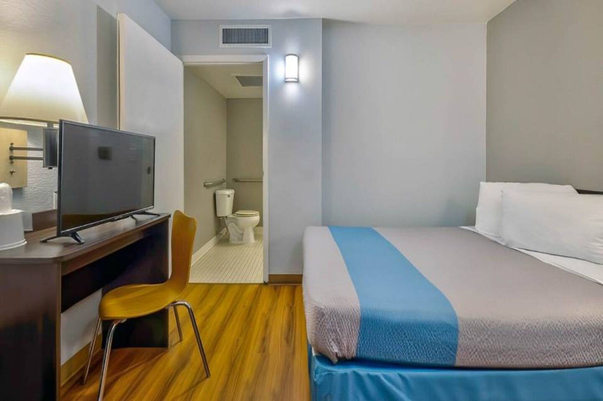 A hotel room with a bed, a desk with a television, a chair, and a bathroom visible through an open door.
