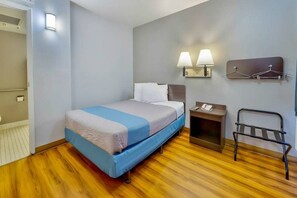A hotel room with a bed, bedside table, lamp, and a coat rack. - 1 QUEEN BED | MOB ACC RI SHWR (TUCUMCARI)