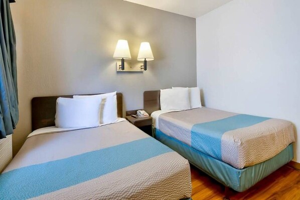A hotel room with two beds, a nightstand, and two wall-mounted lamps.