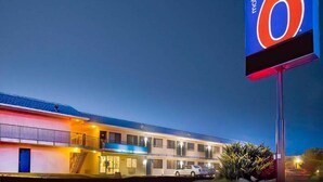 Ein Motel mit einer großen Schautafel, einem Parkplatz und einem Gebäude mit mehreren Fenstern und einem Balkon.