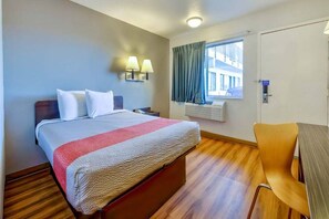 Hotellihuone, jossa on sänky, yöpöytälamput, ikkuna verhoilla, työpöytä ja tuoli.