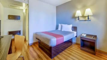 A hotel room with a bed, bedside table, chair, and a desk.