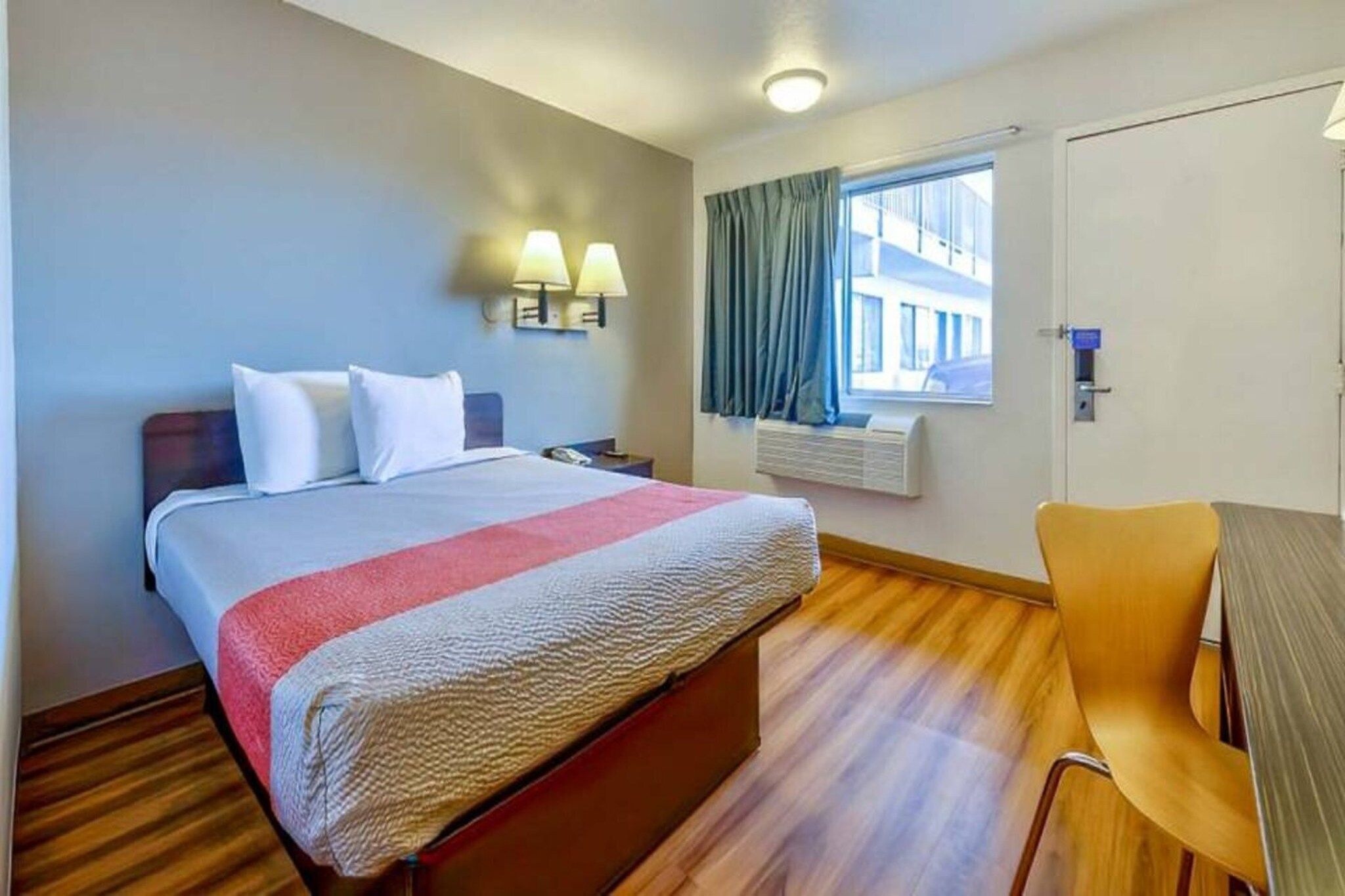 Une chambre d’hôtel avec un lit, des lampes de chevet, une fenêtre avec des rideaux, un bureau et une chaise.