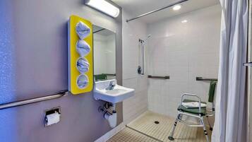 A bathroom with a sink, mirror, shower, and a wheelchair.