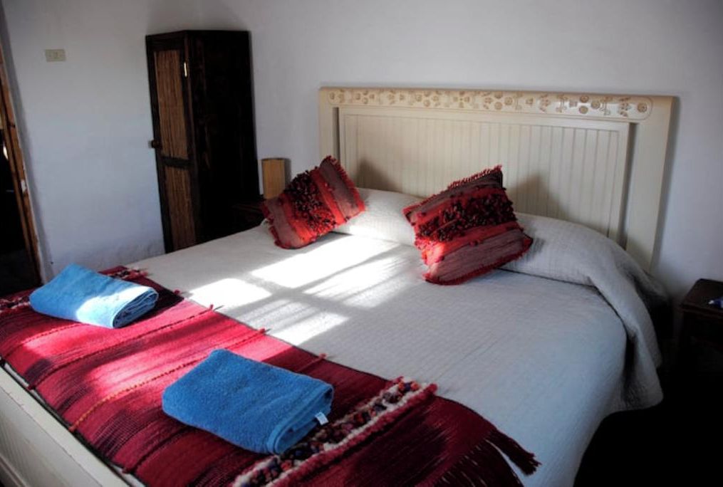 Een bed met een wit hoofdeinde, twee rode kussens en twee blauwe handdoeken.