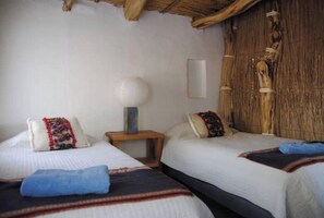 A room with two beds, a nightstand, a lamp, and a wooden wall panel.