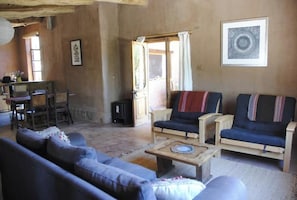 A rustic living room with a sofa, two armchairs, a coffee table, and a dining area with chairs and a table.