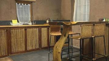 Un espace bar doté d’un comptoir en bois original, de chaises en osier et d’un sol en pierre.