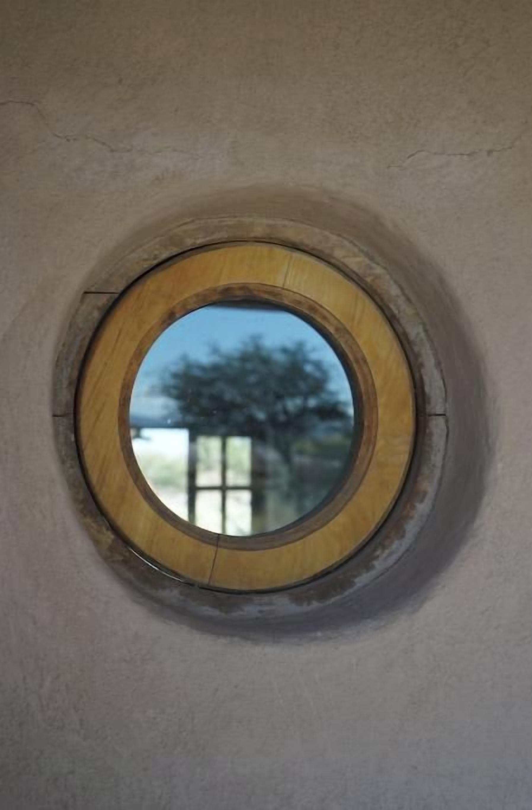 A circular window with a wooden frame, reflecting a tree and a building.