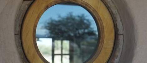 A circular window with a wooden frame, reflecting a tree and a building.