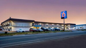 A motel with a large parking lot and a prominent '6' sign. - 1 Queen Bed | Deluxe, Micfridge (Farmington)