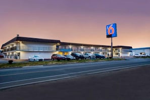 Un motel con un amplio estacionamiento y un llamativo letrero con el número 6.