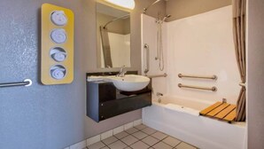 A bathroom with a sink, mirror, shower, and a towel dispenser. - 1 Queen Bed | Deluxe, Micfridge (Farmington)