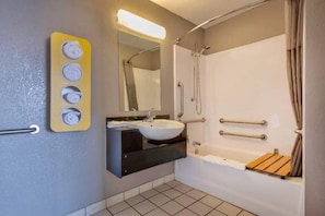 Un baño con lavamanos, espejo, ducha y dispensador de toallas.