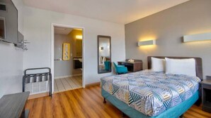 A hotel room with a bed, bedside table, lamp, and a mirror. - 1 Queen Bed | Deluxe, Micfridge (Farmington)