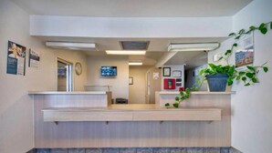 A reception area with a counter, a clock, a television, and a plant. - 1 Queen Bed | Deluxe, Micfridge (Farmington)