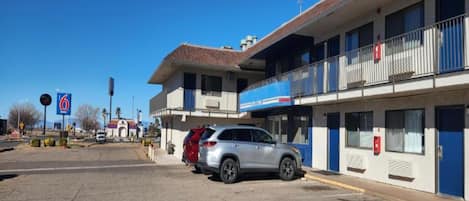 A two-story motel with a parking lot, a red SUV parked in front, and a clear blue sky.