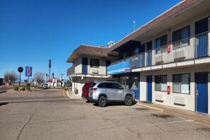 A two-story motel with a parking lot, a red SUV parked in front, and a clear blue sky.