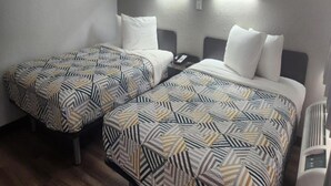 Een hotelkamer met twee bedden, elk voorzien van beddengoed met een patroon, een nachtkastje met een telefoon en wandlampen.