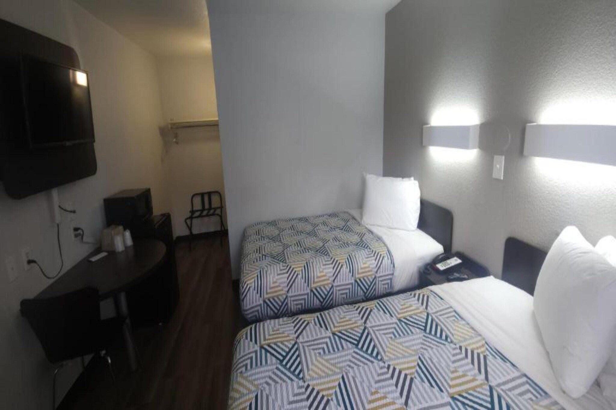Habitación de hotel con dos camas, un escritorio, una silla, un televisor y una lámpara de pared.