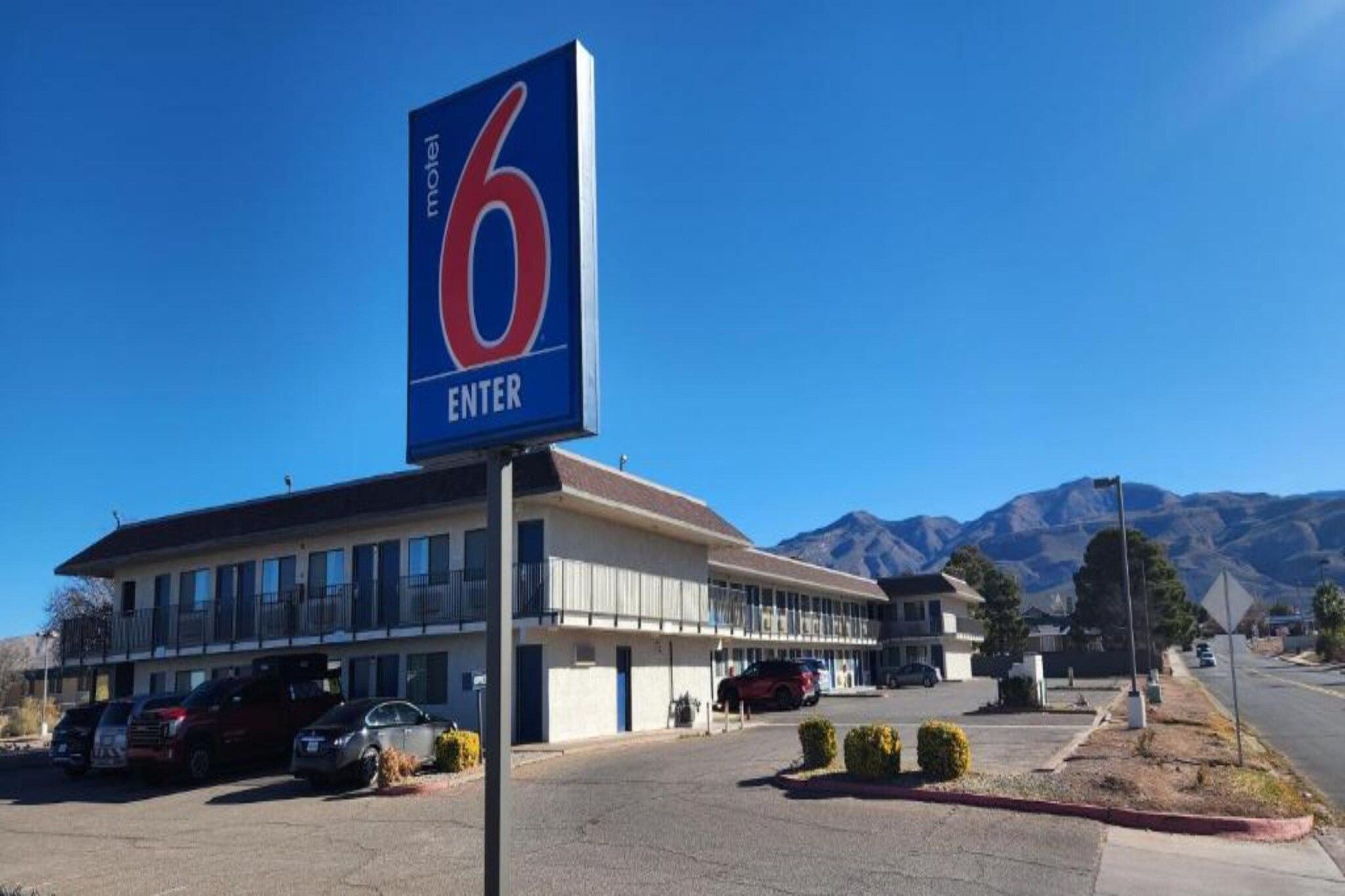 Un motel con un llamativo letrero que dice '6 ENTER', un estacionamiento y montañas al fondo.