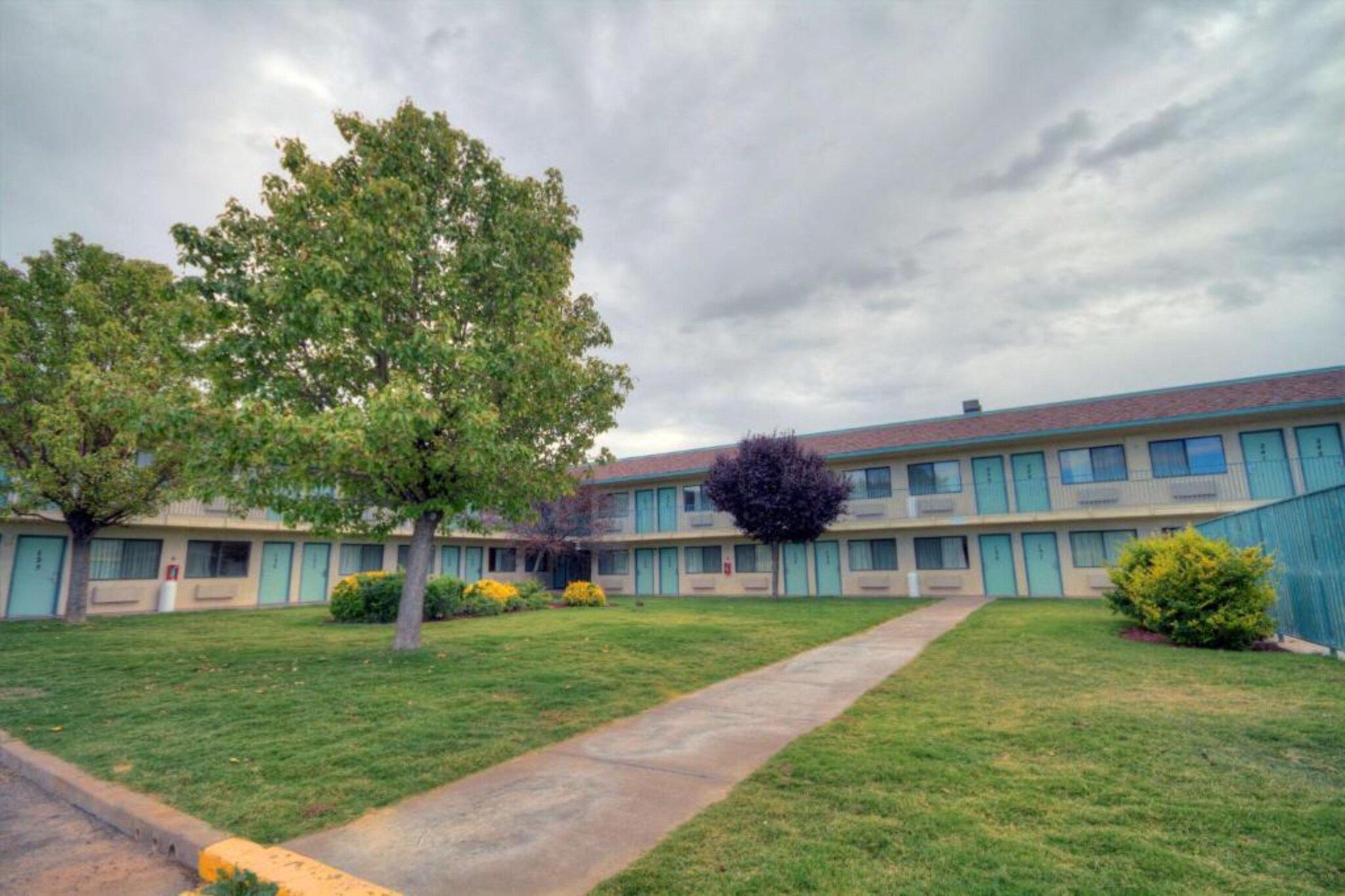 Un motel doté d’une pelouse centrale, d’un sentier et d’une rangée de chambres à la façade uniforme.