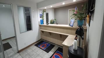 Zona de recepción de un hotel con mostrador, una planta, una bandera y una puerta.