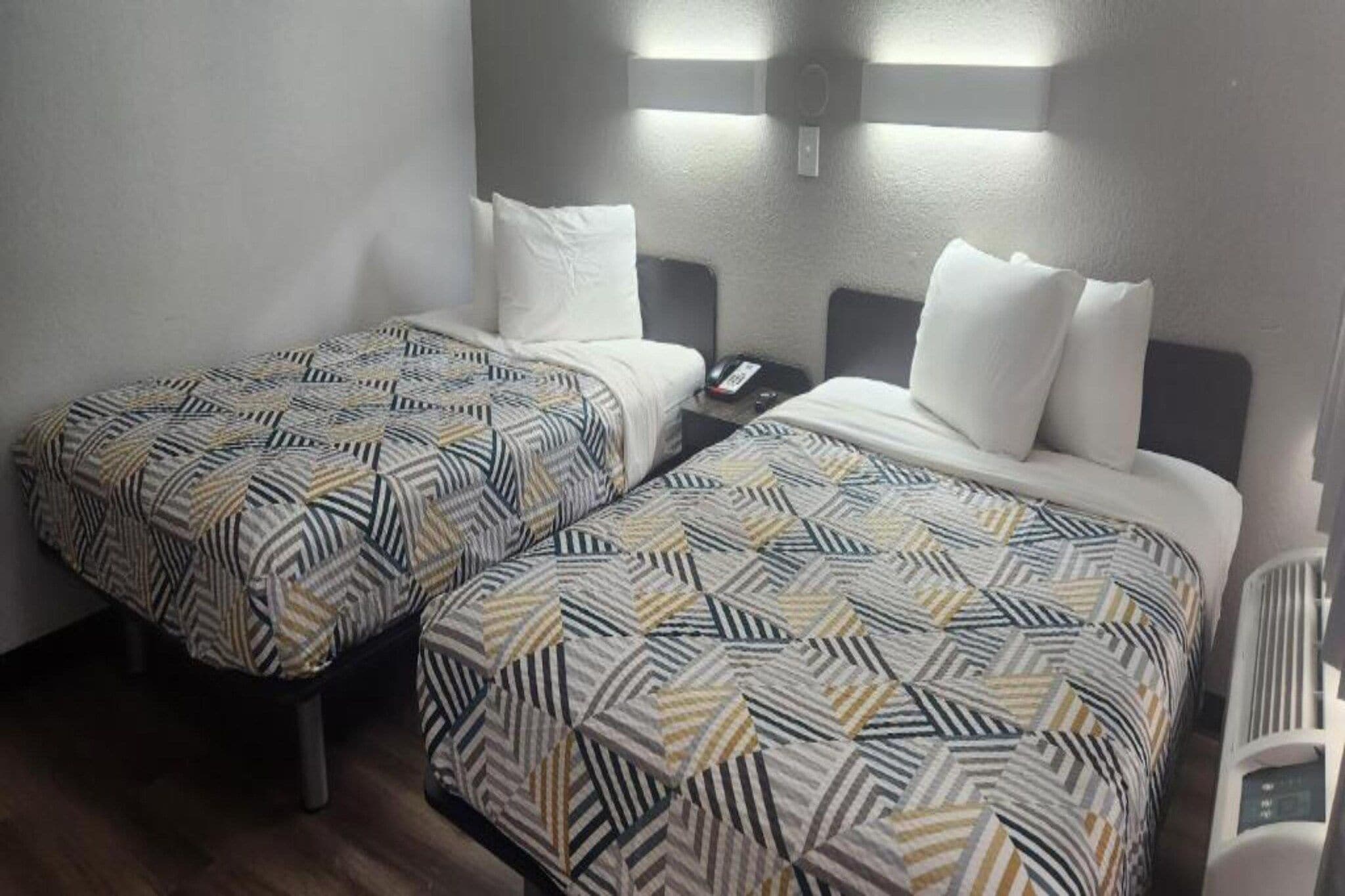 Habitación de hotel con dos camas individuales, cada una con ropa de cama estampada, una mesita de noche con teléfono e iluminación empotrada.