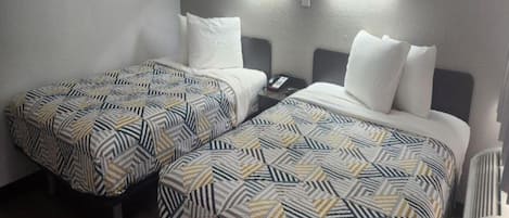 A hotel room with two single beds, each with patterned bedding, a bedside table with a phone, and wall-mounted lighting.