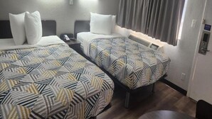 Une chambre d’hôtel avec deux lits, chacun agrémenté de draps à motifs, une table de chevet avec un téléphone et une fenêtre avec des rideaux.
