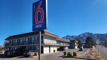 A motel with a prominent '6 ENTER' sign, a parking lot, and a mountain backdrop.