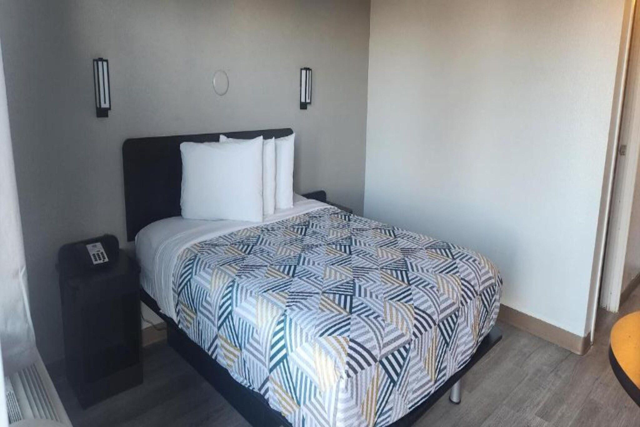 Una habitación estándar de hotel con cama, mesitas de noche y lámparas de pared.