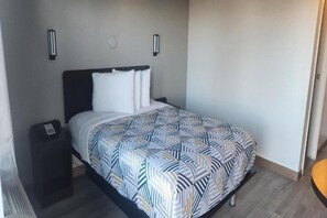 Une chambre d’hôtel avec un lit, une table de chevet et un luminaire fixé au mur.